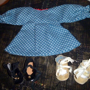 May include: A blue doll dress with white floral patterns, a red trim, and long sleeves. The image also shows three pairs of doll shoes: black Mary Janes, and two pairs of tan shoes with white laces.