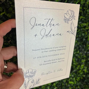 May include: A rectangular wedding invitation card on shimmering off-white paper with dark blue ink. It features the names Jonathan + Juliana, floral line art, and text detailing a ceremony at 3PM, 30th November 2025 at Borcelle Hotel & Ballroom.