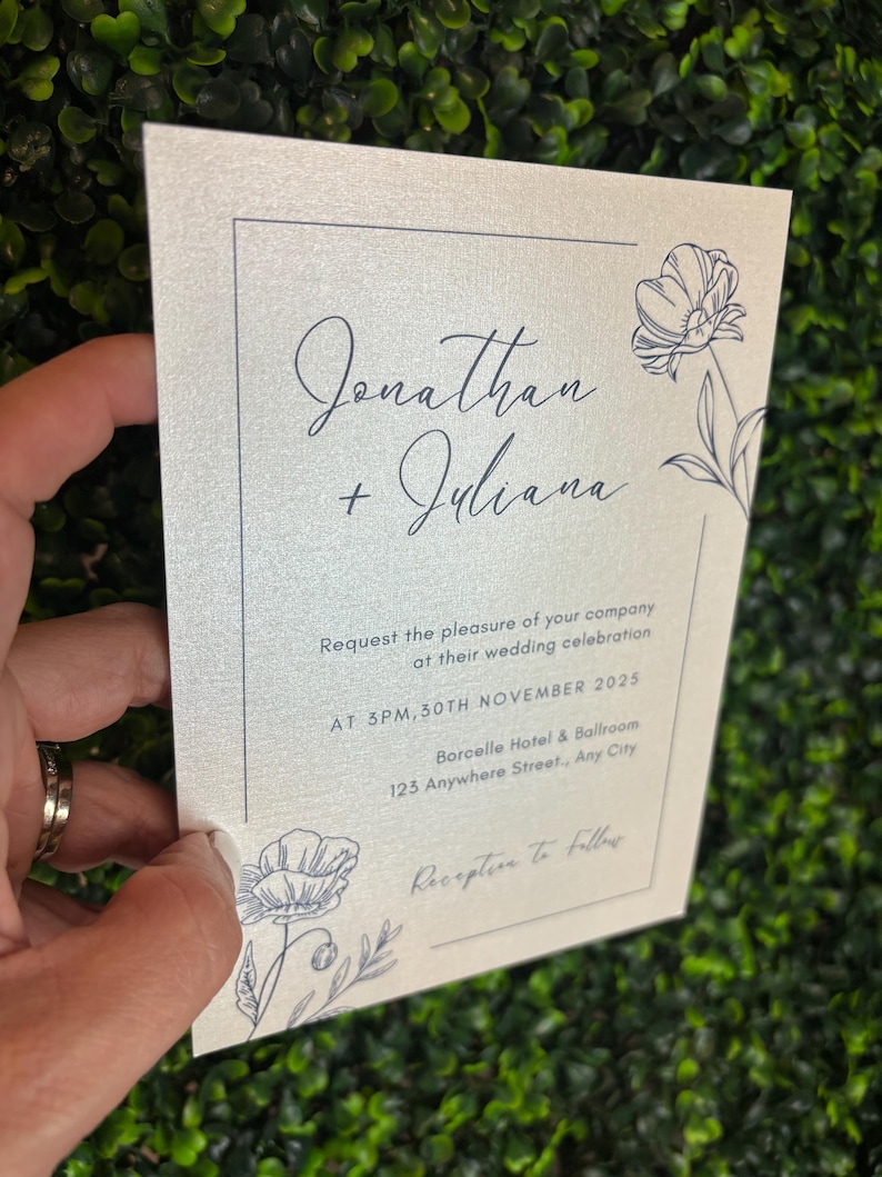 May include: A rectangular wedding invitation card on shimmering off-white paper with dark blue ink. It features the names Jonathan + Juliana, floral line art, and text detailing a ceremony at 3PM, 30th November 2025 at Borcelle Hotel & Ballroom.