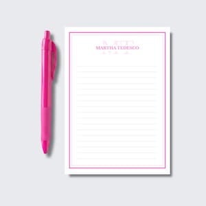 May include: A bright pink retractable ballpoint pen positioned next to a rectangular notepad. The notepad features a double pink border, horizontal lines, and the name MARTHA TEDESCO printed in pink capital letters at the top center.