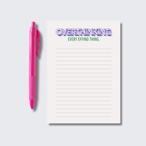 May include: A bright pink retractable ballpoint pen positioned next to a white rectangular notepad. The notepad features horizontal lines and the text OVERTHINKING in purple 3D-style letters, followed by the green text EVERY EFFING THING.