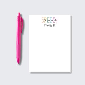May include: A bright pink retractable ballpoint pen positioned next to a white rectangular notepad. The notepad features the word SPEECH in pastel-colored letters, the word therapist in black script, and the name MISS PATTY in black text.