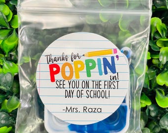 May include: A white circle sticker with the text "Thanks for POPPIN' in! See you on the first day of school! -Mrs. Raza" in colorful letters. The sticker is in a clear plastic bag with a blue and white fidget toy.