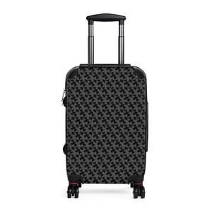 Puede incluir: Una maleta de mano rectangular con un patrón geométrico repetitivo en gris oscuro y negro. El equipaje incluye un asa telescópica de metal plateado, protectores de esquina negros y cuatro ruedas giratorias negras con pequeños detalles rojos.