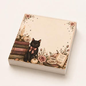 Könnte beinhalten: Ein quadratischer Notizblock mit einem schwarzen Katzenmotiv mit rosa Schleife, umgeben von einem Bücherstapel, einer brennenden Kerze, Kürbissen und Rosen. Die Illustration zeigt Text auf Buchrücken und ein offenes Buch mit Bewitched, Bookish & Caffeinated.