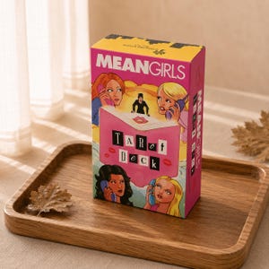 May include: A rectangular Mean Girls tarot deck box featuring a pink book illustration with the text Tarot Deck, surrounded by cartoon characters holding telephones. The box has a yellow top section with the text Mean Girls and a pink main body.
