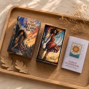 May include: A tarot card deck titled The Living Arcana Tarot with a box featuring a person in a sunset landscape, an open box displaying The Fool card with a person in a red dress, and a white Tarot Guidebook with a sun illustration on the cover.