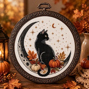 Peut inclure: Une broderie au point de croix circulaire représentant un chat noir assis sur un croissant de lune, entouré de feuilles d'automne, de petites citrouilles et d'étoiles. L'ouvrage est encadré dans un cadre en métal bronze foncé orné.