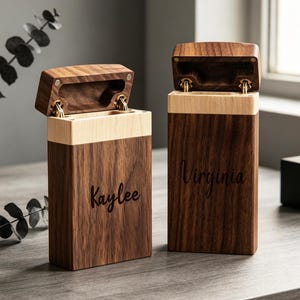 May include: Two rectangular wooden boxes with hinged lids, featuring a dark brown walnut body and a lighter wood accent band at the top. The left box is engraved with the name Kaylee, and the right box is engraved with the name Virginia.