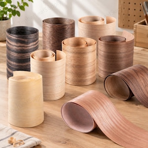 May include: A collection of wood veneer edge banding rolls in various shades, including light beige, medium oak, dark walnut, and black wood grain patterns. The rolls are cylindrical, showing distinct wood textures and natural grain lines.