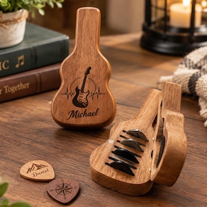 Può includere: Un astuccio in legno a forma di chitarra con coperchio magnetico, inciso con una chitarra elettrica e il nome Michael. Due plettri in legno sono posizionati accanto, uno inciso con una montagna e il nome Daniel, l'altro con una bussola.