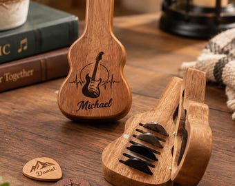 May include: A guitar-shaped wooden case with a magnetic lid, featuring an engraved electric guitar graphic and the name Michael. Two wooden guitar picks are placed nearby, one engraved with a mountain and the name Daniel, the other with a compass design.