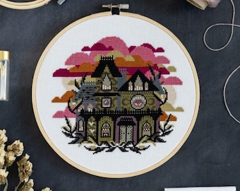 May include: A cross-stitch embroidery hoop featuring a spooky house design with pink and orange clouds. The image includes embroidery supplies: thread spools, scissors, a needle, fabric squares, and a wooden hoop. The color palette is dark with pops of pink.