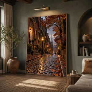 以下が含まれることがあります： 秋の石畳の通りを描いた大きな長方形のウォールアートプリント。レンガ造りの建物、輝く街灯、オレンジ色の葉をつけた木々が並んでいます。遠くには教会の尖塔が見え、地面には落ち葉が散らばっています。