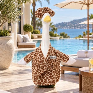May include: A white goose figurine wearing a brown and tan giraffe-patterned bathrobe and a matching shower cap. The bathrobe features a small rectangular name tag on the chest with the name EMMA printed in black capital letters on a silver background.