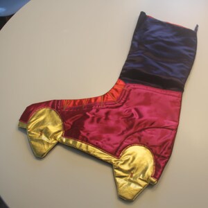 May include: A Christmas stocking shaped like a car, featuring a vibrant color scheme. The main body is a deep magenta, accented with gold-colored wheels and trim. The top portion is a rich navy blue.