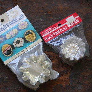 May include: Two vintage baking sets. One package reads "6 PIECE INDIVIDUAL tart & pastry mold set" with illustrations of baked goods. The other package reads "6 pcs TARTLET MOLDS" and is made of aluminum.