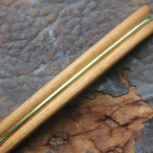 May include: A wooden and brass hair clip with a gold-colored metal strip running down the center.