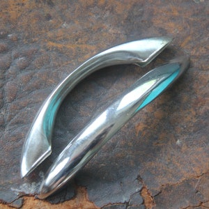 May include: Two silver-toned metal cabinet door handles. The handles are shaped like a half-circle and have a smooth, polished finish.