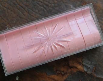 May include: A clear plastic box with a pink, starburst-shaped design inside. The box is empty.