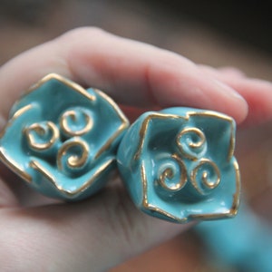 May include: Two turquoise blue ceramic drawer pulls with gold trim and a swirling design.