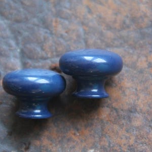 May include: Two blue ceramic cabinet knobs with a smooth, glossy finish. The knobs are round with a slightly raised center and a short stem.