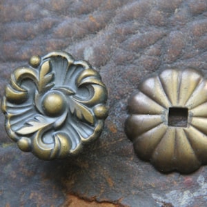 May include: Two antique brass decorative hardware pieces. One is a round, ornate piece with a floral design. The other is a round, fluted piece with a hole in the center.