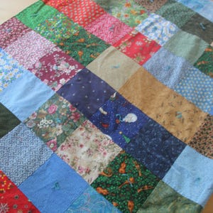 May include: A patchwork quilt made of various fabrics in different colors and patterns. The quilt is made up of squares of fabric sewn together to create a larger design. The quilt is a beautiful example of handmade craftsmanship.