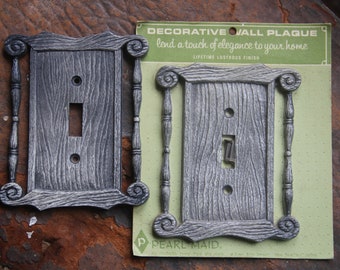 May include: Two decorative wall plaques with a woodgrain finish and a switch plate design. The plaques are packaged on a green card with the text "DECORATIVE WALL PLAQUE lend a touch of elegance to your home LIFETIME LUSTROUS FINISH PPEARL MAID."