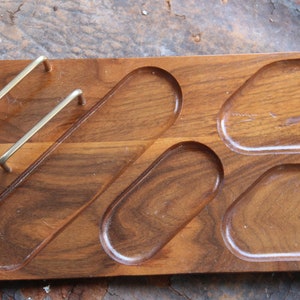 May include: A wooden tray with four oval-shaped compartments and two brass handles. The tray is made of dark wood and has a smooth finish.
