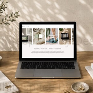 Puede incluir: Un portátil plateado muestra un sitio web con el texto "Beautiful websites. Distinctive brands." en la pantalla. El portátil está sobre un escritorio de madera junto a un jarrón de cerámica, un vaso de agua, un cuaderno, un bolígrafo y clips.