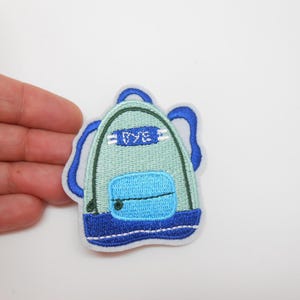 Peut inclure: Écusson brodé en forme de sac à dos, principalement vert clair avec des détails bleus. Le mot "BYE" est brodé en haut. L'écusson est posé sur un fond blanc. Idéal pour personnaliser des vêtements ou accessoires.
