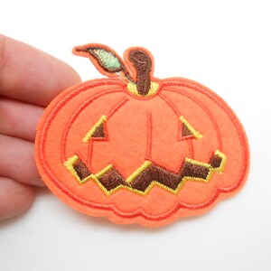 Peut inclure: Applique thermocollante en forme de citrouille orange en feutre avec un visage de citrouille sculptée cousu. La citrouille a une tige en feutre vert.