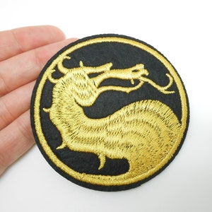 Peut inclure: Écusson rond noir avec un motif de dragon brodé en or. Le dragon est dans un cadre circulaire. L'écusson est probablement destiné aux vêtements ou aux accessoires, pour un élément décoratif.