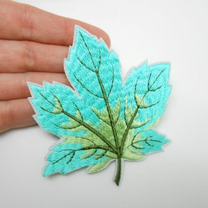 Peut inclure: Écusson de feuille brodée dans les tons de turquoise, vert et vert clair. La feuille a une bordure blanche et des coutures détaillées, créant un aspect texturé. Ce patch décoratif est idéal pour ajouter une touche de nature aux vêtements ou accessoires.