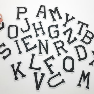 Peut inclure: Un ensemble de lettres en feutre noir et blanc, comprenant l'alphabet de A à Z. Les lettres sont dans un style de police classique et gras.