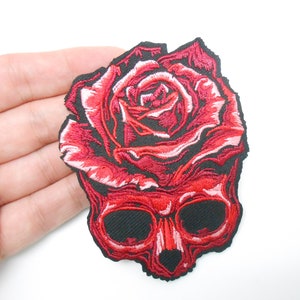 Peut inclure: Patch thermocollant brodé rouge représentant un crâne surmonté d'une rose rouge.