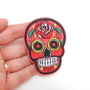 Peut inclure: Écusson brodé en forme de tête de mort mexicaine, fond rouge et contour noir. Le crâne a des yeux jaunes et noirs, une rose sur le front et un sourire blanc. Un article décoratif.