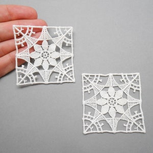 Peut inclure: Deux carrés en crochet blanc avec un motif floral au centre. Les carrés sont délicats et complexes.