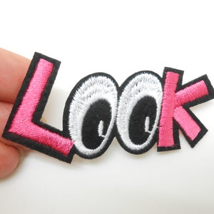 Peut inclure: Patch thermocollant brodé rose avec le mot "LOOK" en lettres blanches et deux grands yeux noirs avec des pupilles blanches.
