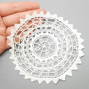 Peut inclure: Un napperon en crochet blanc avec un motif circulaire et un bord festonné.