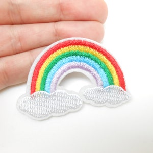 Peut inclure: Un patch brodé représentant un arc-en-ciel coloré avec des nuages blancs. L'arc-en-ciel a des rayures rouges, orange, jaunes, vertes, bleues, indigo et violettes.