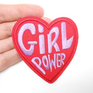 Peut inclure: Un écusson rouge en forme de cœur avec les mots "GIRL POWER" brodés en lavande. L'écusson est en tissu et a une bordure cousue. Le design est simple et audacieux, adapté aux vêtements ou aux accessoires.