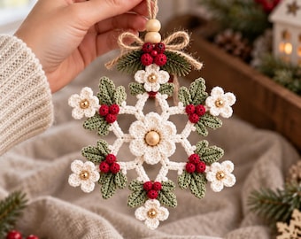May include: A crocheted snowflake ornament featuring cream-colored flowers, dark green leaves, and clusters of small red berries. The center of each flower has a gold bead, and the ornament is topped with a jute twine loop and wooden beads.