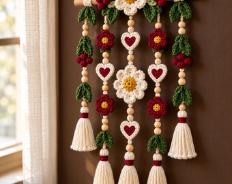 May include: A wall hanging featuring a wooden dowel with five hanging strands of crocheted flowers, hearts, and green leaves. The design includes cream, red, and yellow yarn, wooden beads, and cream-colored tassels at the bottom of each strand.