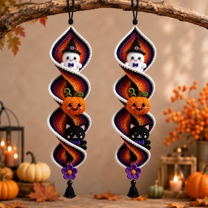 May include: Two hanging spiral decorations made of crocheted yarn in a gradient of purple, orange, and yellow. Each features a white ghost with a black hat, an orange pumpkin, a black cat, and a purple flower with a black tassel at the bottom.