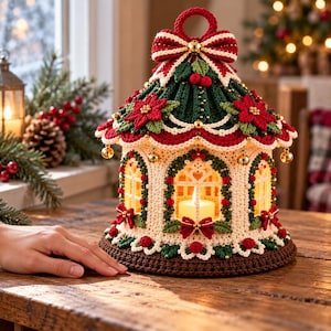 May include: A crocheted lantern with a cream-colored base, dark green roof, and red poinsettia accents. The structure features arched windows, small gold bells hanging from the scalloped edge, and a top bow with a central gold bell.