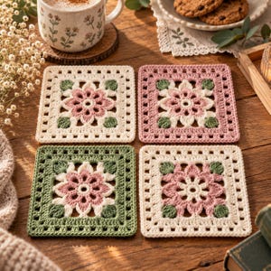 May include: Four square crochet coasters featuring a central floral motif in pink, cream, and sage green. Each coaster displays a detailed petal design surrounded by a geometric border, showcasing intricate yarn work in soft, muted color palettes.
