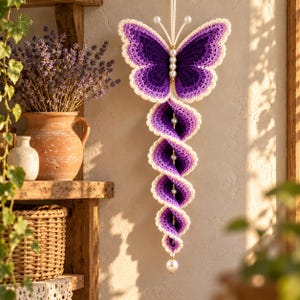 May include: A hanging crochet decoration featuring a purple butterfly at the top with white-edged wings and antennae. Below the butterfly, a spiraling, multi-layered purple crochet tail descends, accented with white pearls along the center spine.
