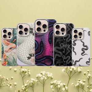 Op de afbeelding: Vijf smartphonehoesjes op een rij, elk met verschillende slangenmotieven. De ontwerpen omvatten een realistische oranje slang, een witte slang met bloemen, een paars en zwart raster met slangen, een zwart-witte lijntekening en een wit hoesje met zwarte slangensilhouetten.